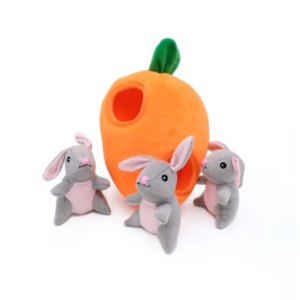 Three grey and pink plush rabbits surround a Zippy Burrow® - Bunny 'n Carrot with a green top and a hole in the side.