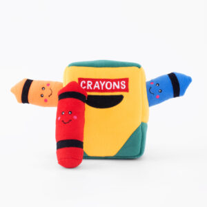 A yellow and green plush toy shaped like a crayon box with the word "CRAYONS" on it. Three plush crayons, one orange, one red, and one blue, with smiling faces stick out from the box.