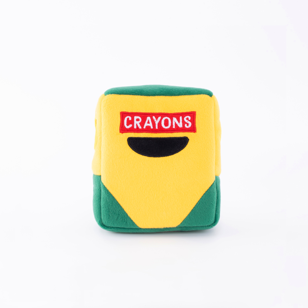 A plush toy resembling a yellow and green crayon box with a red label marked 