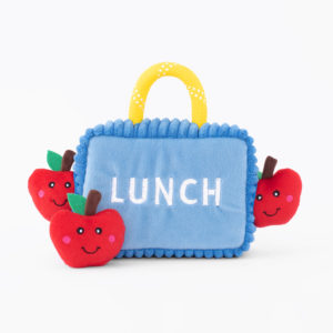 A soft fabric toy lunchbox with "LUNCH" embroidered on it, featuring a yellow handle and surrounded by three smiling apple plushies.