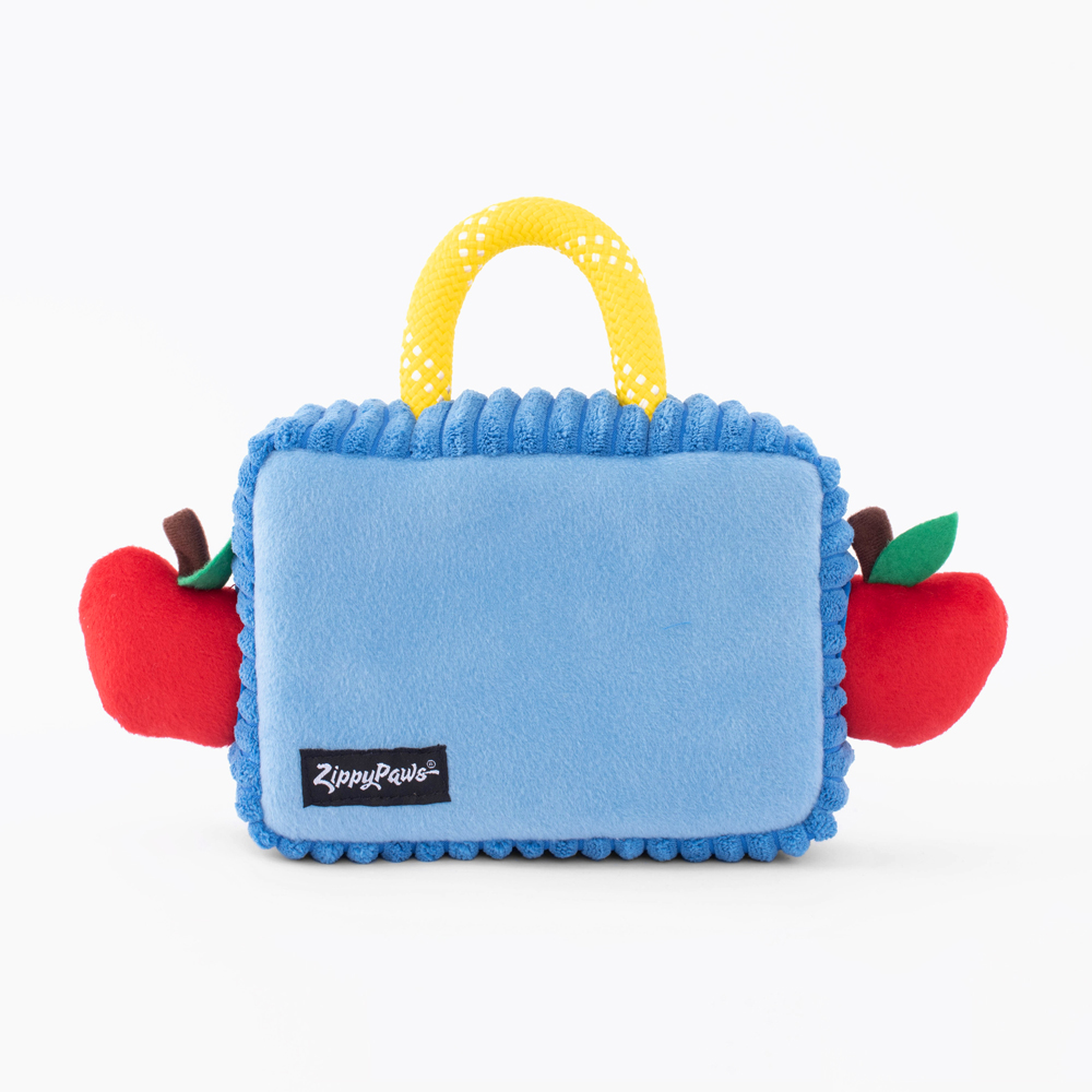 A rectangular blue soft toy with a yellow handle and red stuffed apples attached on the sides. The label reads 