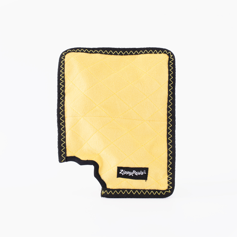 A yellow rectangular dog toy with black stitched edges and a label reading "Zippy Paws." One corner appears to be chewed off.