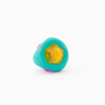 A small, round object with a turquoise outer layer, a yellow polygonal transparent center, and visible pink details at the back against a white background.