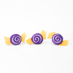 Three purple and yellow fabric candy-shaped decorations with a swirl pattern on a white background.