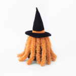 A plush toy with orange fuzzy hair wearing a black witch hat with an orange band, placed against a plain white background.