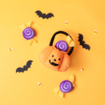 A Halloween Burrow® - Trick-or-Treat Basket filled with candy, surrounded by bat silhouettes, purple candies, and candy corn on a yellow background.