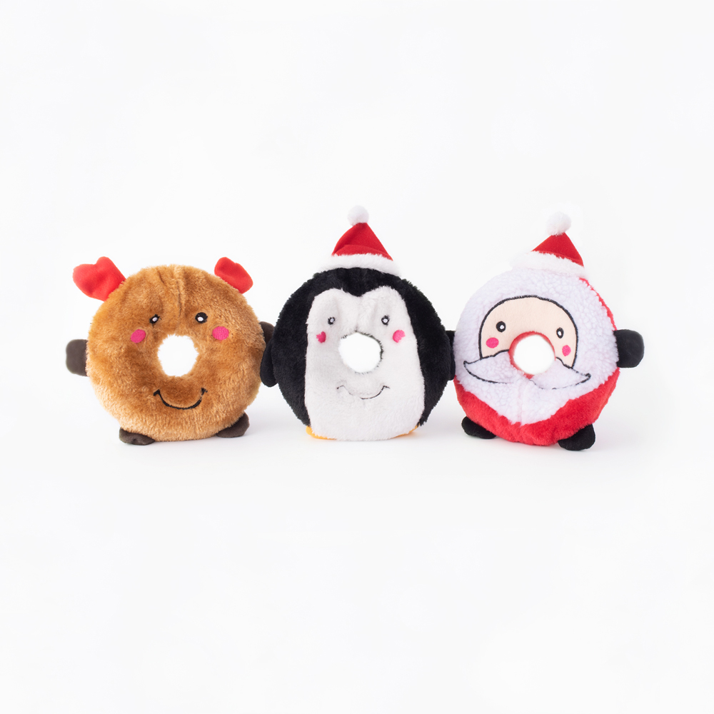 Three donut-shaped toys: brown reindeer with antlers, black and white penguin with a red hat, and Santa Claus with a red hat. All have round bodies and smiling faces. They are placed against a white background.