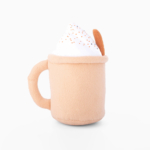 Plush toy shaped like a beige mug of hot beverage topped with white foam and brown sprinkles, with a handle on the left and a cookie on the right.
