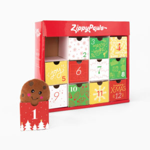 A red ZippyPaws advent calendar with 12 numbered doors. Door 1 is open, revealing a plush smiling cookie toy. The doors are decorated with festive designs and colors.