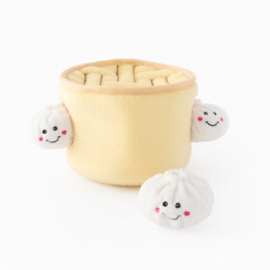 Plush toy of a yellow basket holding two smiling dumplings, with another dumpling outside the basket on a white background.