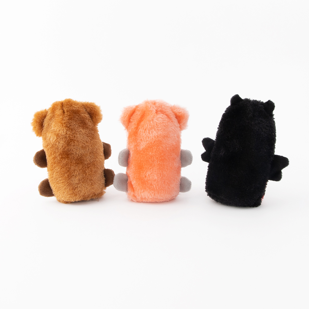 Three plush toys resembling animals are lined up with their backs facing the camera. The toys are brown, pink, and black in color.