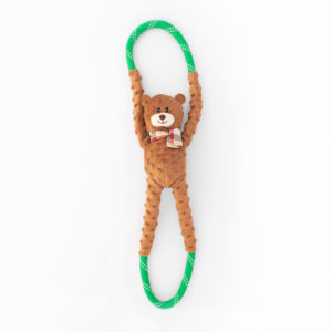 A brown teddy bear toy with a plaid bow is attached to a green and white rope with loops on both ends. The bear appears to be hanging from the rope by its arms and legs.