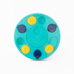 A circular, turquoise-colored pet puzzle toy with "SmartyPaws Puzzler Teal" written on it. The toy features blue and yellow movable compartments for hiding treats.