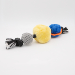 A three-section dog toy with gray, yellow, and blue plush balls connected by black and white fabric ropes is laid out on a plain white background.