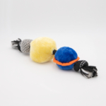 A colorful dog toy consisting of three plush balls in yellow, gray, and blue, connected by a black-and-white braided rope.