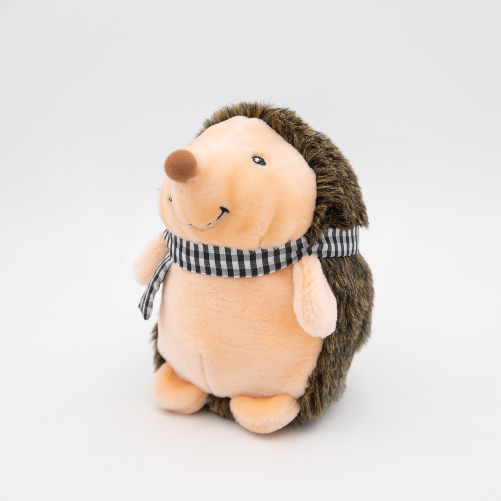 A plush toy hedgehog with a soft beige front, fluffy brown back, and a black-and-white checkered scarf around its neck, standing against a plain white background.