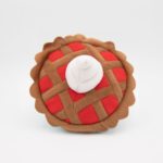 A plush toy shaped like a pie with a lattice crust design and a dollop of white cream on top.