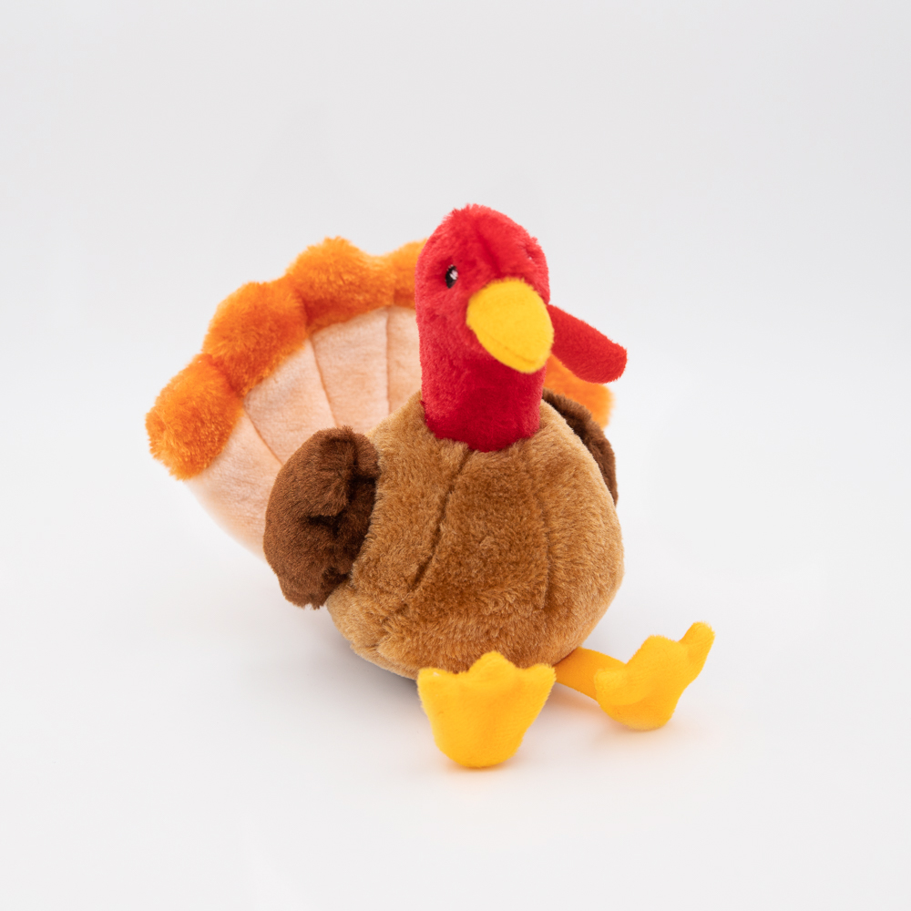 A plush toy shaped like a turkey, featuring a red head, yellow beak, orange and brown wings, and yellow feet, is placed against a plain white background.