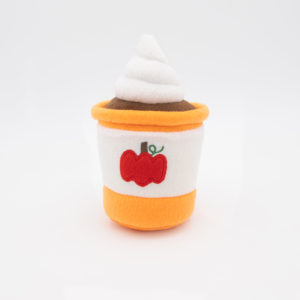 A plush toy shaped like a dessert cup with white and orange layers, topped with white frosting, and featuring an embroidered red apple on the front.