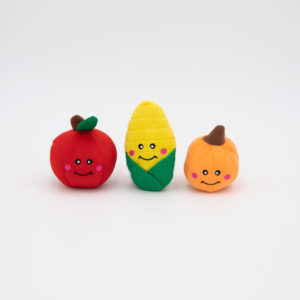 Three plush toys with smiley faces: a red apple, a yellow corn cob with green husk, and an orange pumpkin.
