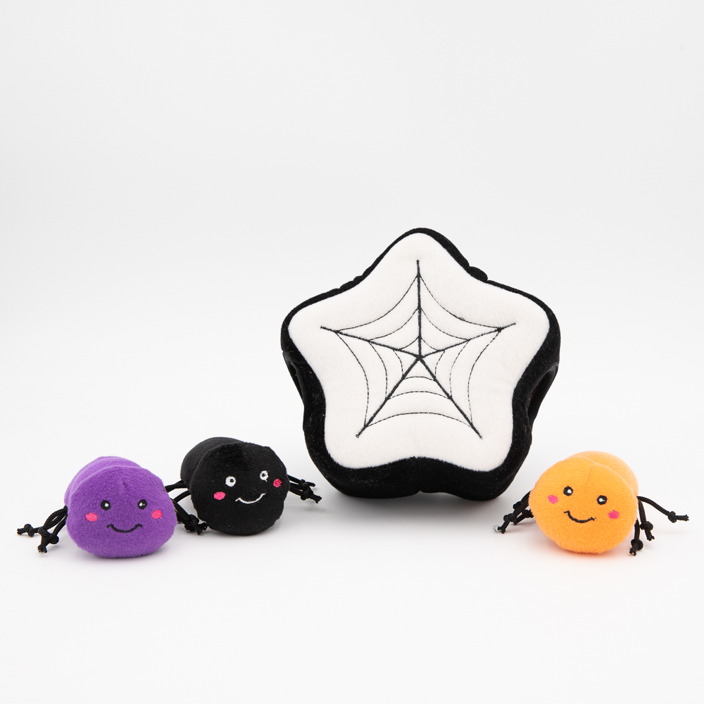 A black-and-white star-shaped plush toy with a spiderweb pattern is accompanied by three small, round, colorful plush spiders in purple, black, and orange. This product is known as Halloween Burrow® - Spider Web.