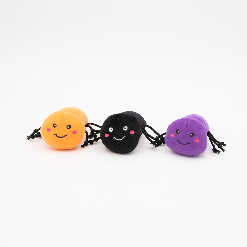 Three small, round plush toys in orange, black, and purple with smiling faces and dangling legs, arranged in a row on a white background.