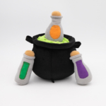 A Halloween Burrow®  - Witch's Brew filled with green substance and three gray plush potion bottles, each with a different colored label (orange, green, purple), surrounding the cauldron.
