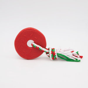 A red rubber donut-shaped dog toy with a white and green braided rope tassel attached.