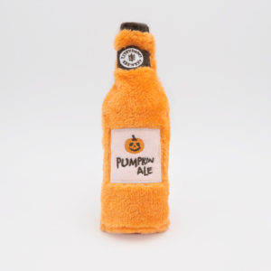 A plush toy resembling a pumpkin ale bottle with an orange fuzzy texture and a label that reads "Pumpkin Ale" with a small pumpkin icon.