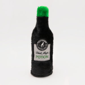 A black plush toy shaped like a bottle with a green top. The label reads "Fluffypaws Distillery, Black Magic Potion.