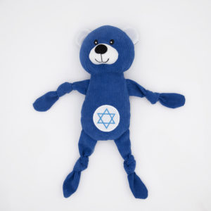 A blue stuffed bear with white ears, featuring a smiling face and a Star of David symbol on its stomach, lying on a white surface.