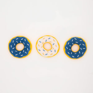 Three plush donuts with frosting and sprinkles, two with blue frosting and one with white frosting, arranged in a row on a plain white background.