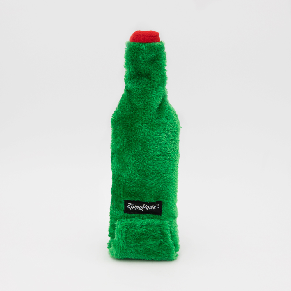 A plush, green dog toy shaped like a bottle with a red cap and a small black label reading 