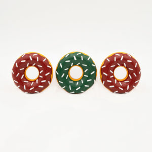 Three toy donuts with white sprinkles, two are brown and one in the middle is green, are aligned in a row against a plain white background.