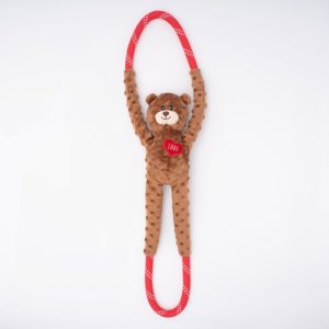 A plush teddy bear with a textured surface and outstretched arms, holding a red heart labeled "Love", attached to a red, polka-dotted elastic loop.