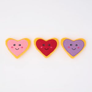 Three heart-shaped plush toys with smiling faces and pink, red, and purple colors, lined up horizontally on a plain white background.