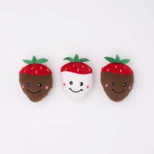 Three strawberry-shaped plush toys with smiling faces arranged in a row. The left and right strawberries are brown, and the center one is white.