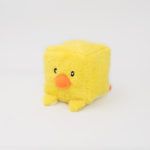 A small, plush yellow square toy with an orange beak and simple black eyes, resembling a chick, against a plain white background.