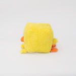 A fluffy yellow square plush toy with an orange beak and feet, resembling a simplified duck, against a plain white background.