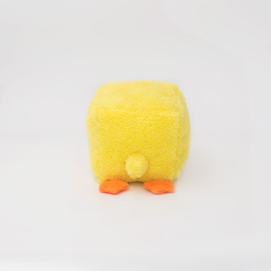 A small, square-shaped yellow plush toy resembling a chick, facing away with orange feet and a small tail visible against a plain white background.