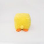 A small, square-shaped yellow plush toy resembling a chick, facing away with orange feet and a small tail visible against a plain white background.