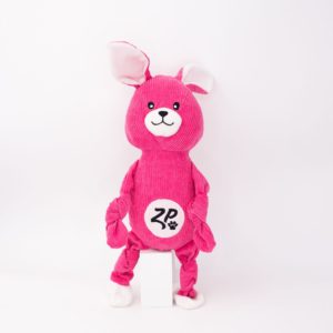 A pink plush dog toy with floppy ears, a smiling face, and knotted limbs. The stomach area features a logo with the letters "ZP" and a paw print.