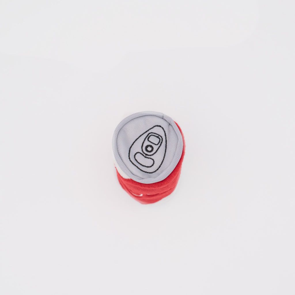 A soft fabric toy resembling a closed soda can, with a gray top and a red body, placed on a white background.