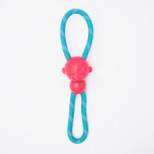 A red rubber monkey head with a blue and white braided rope looped through it, designed as a dog toy, on a white background.