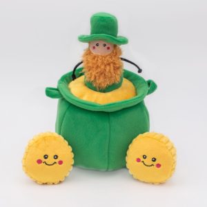 A stuffed toy leprechaun with an orange beard and green hat sits in a green plush pot. Two smiling yellow plush coins are placed in front of the pot.