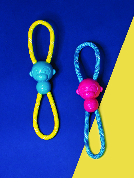 Two colorful dog toys with monkey-shaped ends and looped ropes. The toy on the left has a blue monkey and yellow rope, and the toy on the right has a pink monkey and blue rope, against a blue and yellow background.