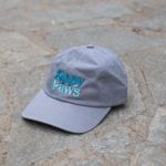 A grey baseball cap with the words "Zippy Paws" embroidered in turquoise on the front sits on a stone pavement.