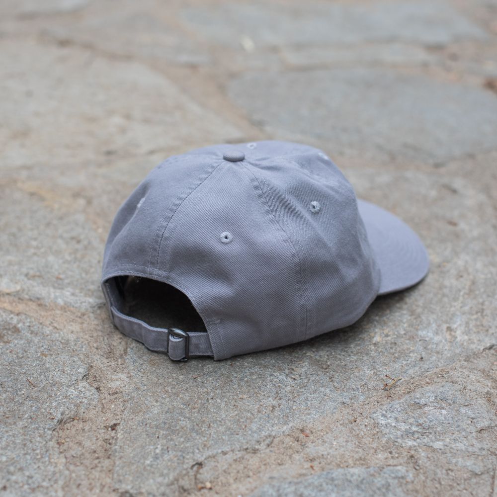 A gray baseball cap lies on a stone surface, shown from the back with the adjustable strap and buckle visible.