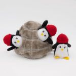 Three plush penguin toys with red hats; two emerging from a brown, plush igloo, and one standing outside.