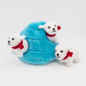 A plush toy showing a blue igloo with three small white polar bears wearing red scarves peeking out of and surrounding the igloo.